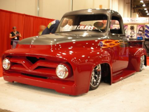 1998 Ford Crown Victoria - dark-red and gray lowered classic pickup with flame graphics displayed at an automotive trade show.