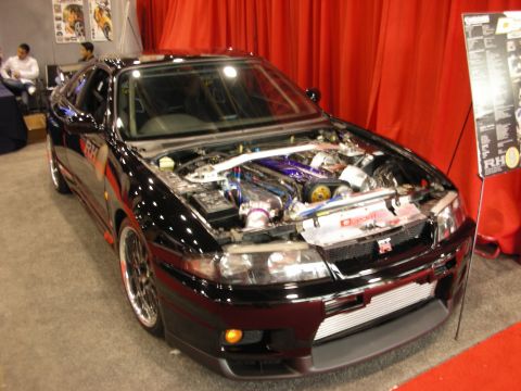 1998 Ford Crown Victoria - black Nissan Skyline GT-R sits with its hood open revealing a polished turbocharged engine bay against a red backdrop.