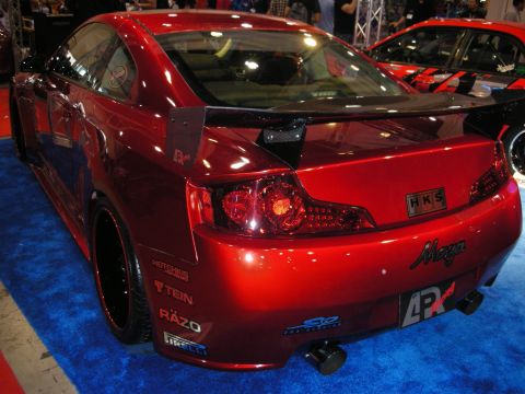 1998 Ford Crown Victoria - Rear three-quarter view of a red modified coupe with a rear wing and HKS and Maya decals on a blue show-floor carpet.