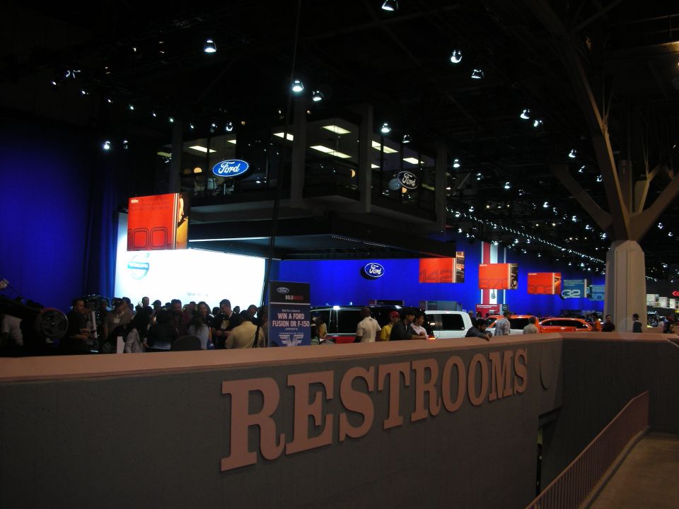Interior trade show hall with Ford booth and large RESTROOMS sign