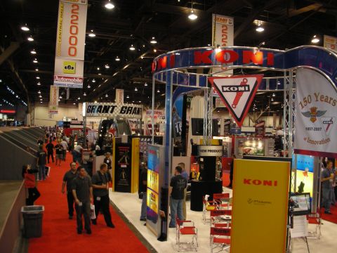 1998 Ford Crown Victoria - crowded trade-show aisle with red carpet lined by KONI, Grant, and other vendor booths under high ceilings.