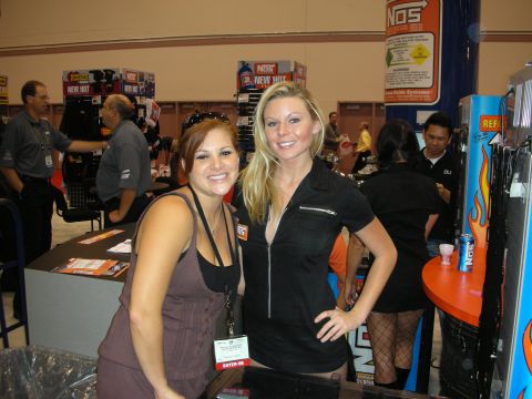1998 Ford Crown Victoria - Two smiling women pose for the camera in front of a NOS energy drink display at a busy trade show booth.