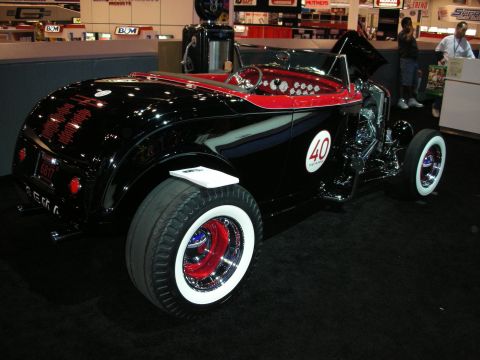 1998 Ford Crown Victoria - black-and-red highboy hot rod roadster with whitewall tires and a number 40 roundel displayed at an indoor show.