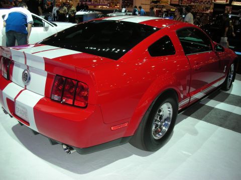 1998 Ford Crown Victoria - red Ford Mustang Shelby with white racing stripes and drag wheels shown rear-three-quarter at an indoor show.