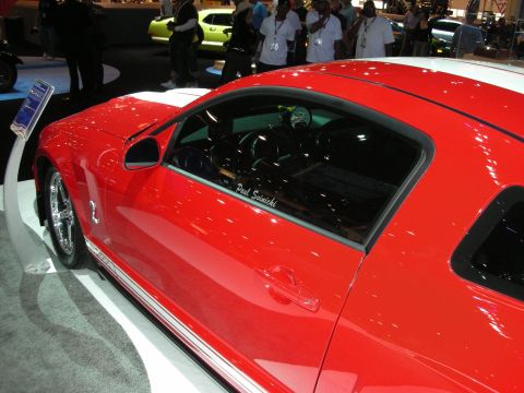 1998 Ford Crown Victoria - red Ford Mustang with a white stripe shows a signed side window as a crowd of attendees stands behind it.