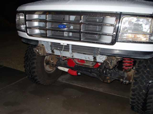 Front of white lifted Ford with chrome grille, red coil springs and big off-road tires at night