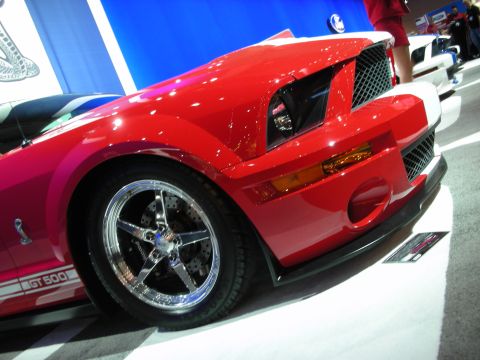 1998 Ford Crown Victoria - Front corner of a red GT500 showing the hood vent, amber side marker, chrome wheel and GT 500 rocker graphic at a show.