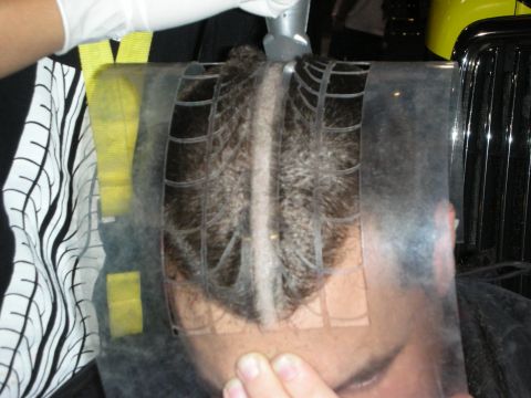 1998 Ford Crown Victoria - clear gridded stencil template is held against the back of a seated man's head to guide a patterned haircut design.