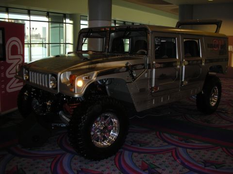 1998 Ford Crown Victoria - lifted silver Hummer H1 wagon with chrome wheels, oversized off-road tires and CNN livery displayed on patterned carpet.