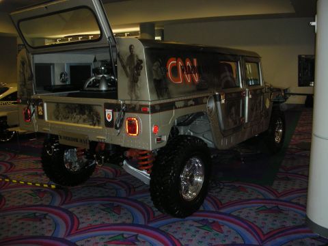 1998 Ford Crown Victoria - Rear three-quarter of a lifted Hummer H1 with camouflage and soldier graphics, CNN lettering and chrome wheels on show carpet.