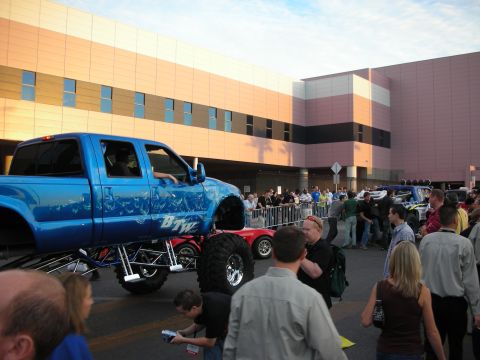 1998 Ford Crown Victoria - blue lifted pickup truck on tall custom suspension is parked among a crowd of spectators outside a convention center.