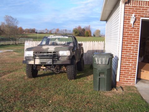 1988 Ford Bronco - This camouflaged Ford Bronco is parked in front of a garage with a trash can nearby.