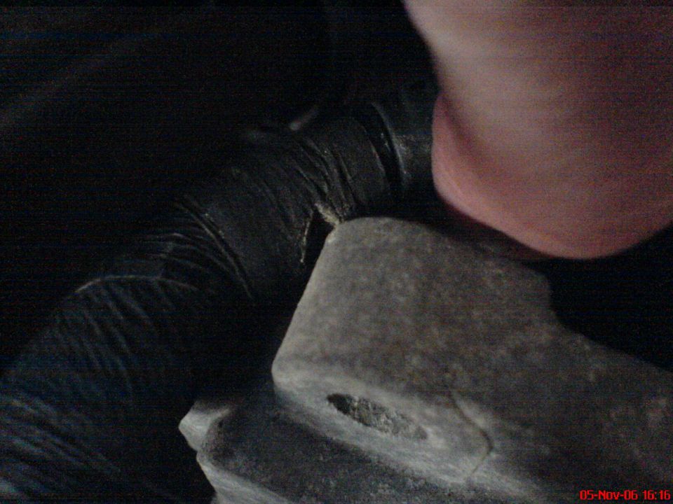 Hand holding a gray engine part near a black hose