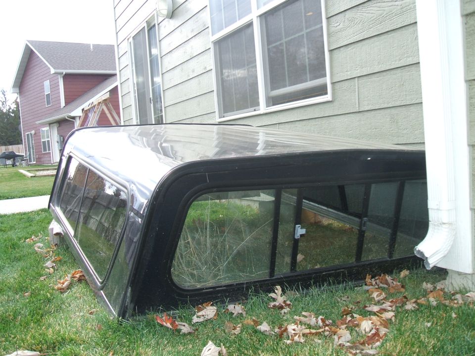 Black truck bed cap on grass next to a house