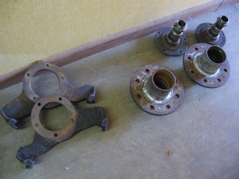 1974 Ford F-100 - Various rusty metal components, including hubs and what appear to be steering knuckles, are scattered on the ground.