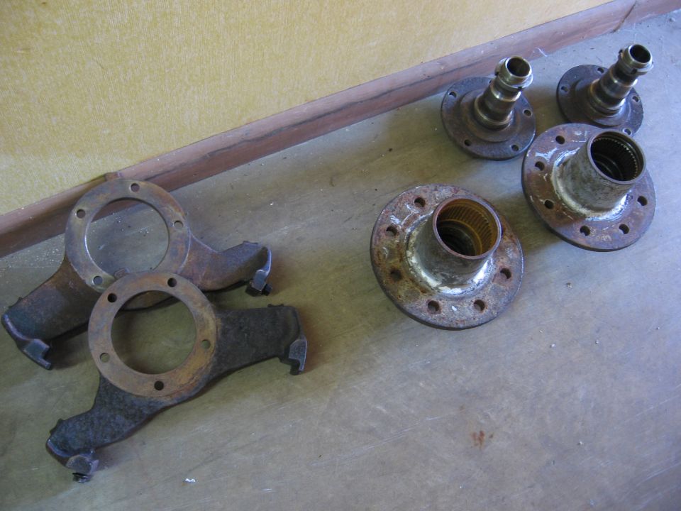 Several rusty metal parts, possibly from a vehicle's axle or suspension, laid out on a concrete floor