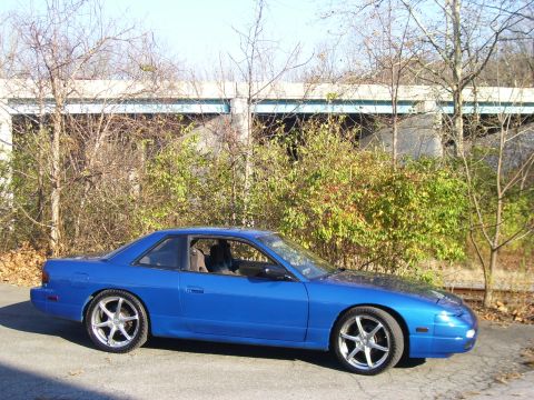 1993 Nissan 240SX - A blue coupe with aftermarket wheels is parked outdoors in front of a building and trees.