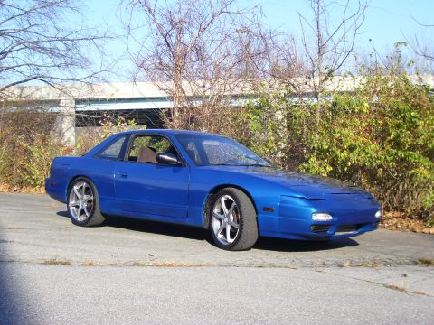 1993 Nissan 240SX - A blue 1993 Nissan 240SX coupe is parked on an asphalt surface with trees and a building in the background.