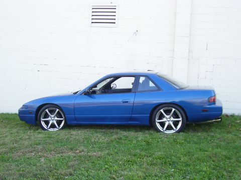 1993 Nissan 240SX - A blue 1993 Nissan 240SX coupe is shown from the side, parked on grass in front of a white wall.