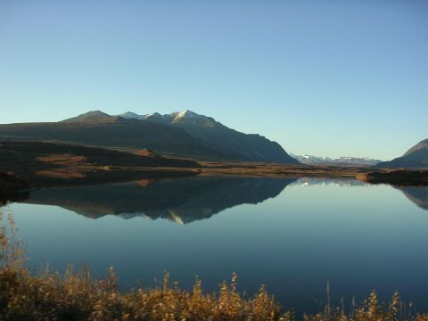 1982 Chevrolet C/K Pickup - A mountain landscape is perfectly reflected in the calm waters of a lake, with snow-capped peaks in the distance.