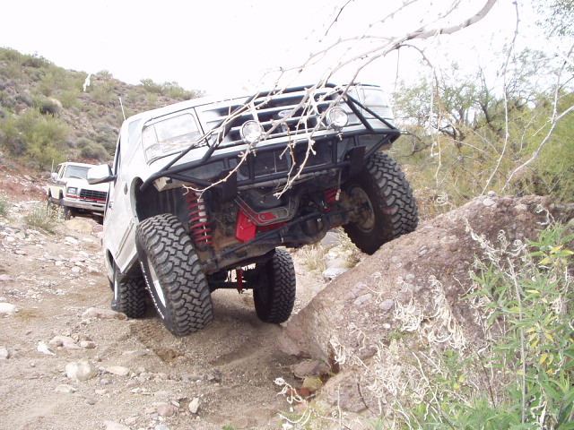 White Ford Bronco with tube bumper flexing over a boulder on a desert trail