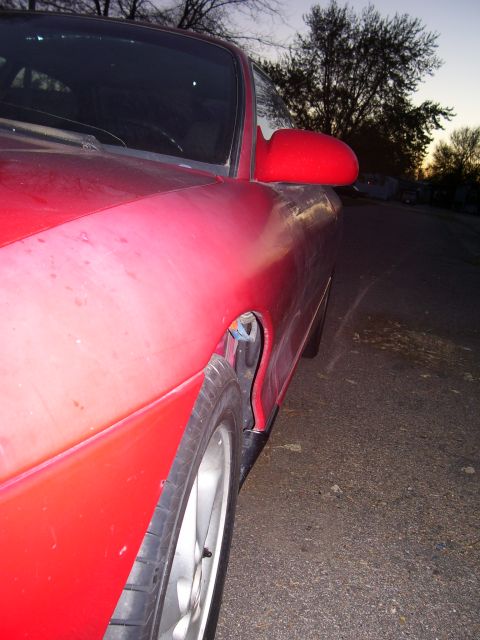 1993 Mazda MX-6 - The front quarter panel and side mirror of a red sports coupe are visible against a dusky sky.