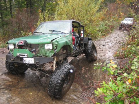 1990 Ford Bronco - A modified green off-road vehicle tackles a challenging trail with another vehicle visible in the background.