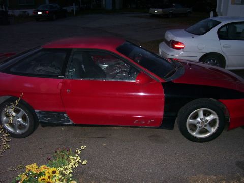1993 Mazda MX-6 - This red and black coupe is seen from the side, with its interior covered in plastic. Two other vehicles are parked nearby.