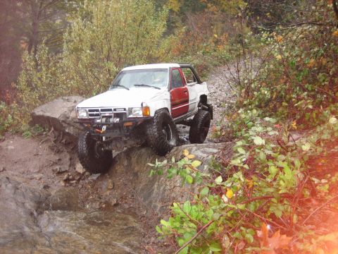 1990 Ford Bronco - Modified pickup truck with large tires navigating a rocky trail in an off-road setting.