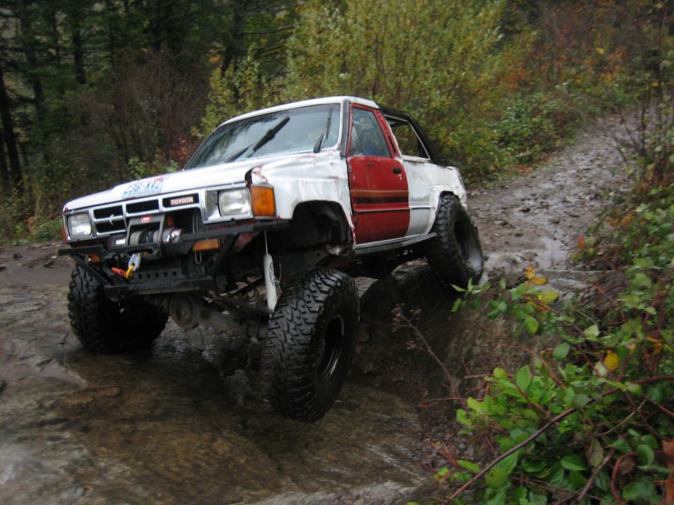 Modified Toyota pickup truck with large tires driving on a muddy, rocky trail