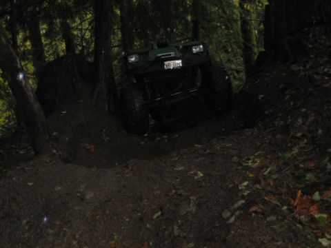 1990 Ford Bronco - A green off-road vehicle navigates a steep, muddy incline surrounded by trees.