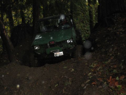 1990 Ford Bronco - A green off-road vehicle is seen on a muddy trail surrounded by trees, with its license plate visible.