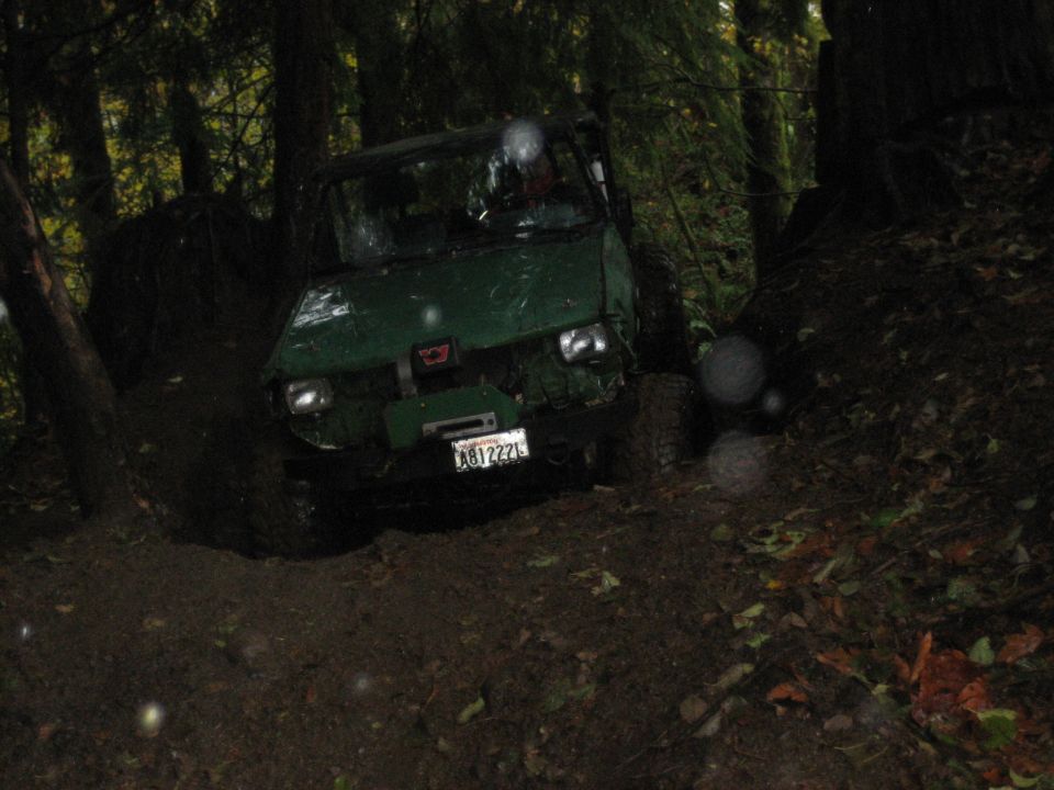 Green off-road vehicle with license plate AB1222L navigating a muddy forest trail