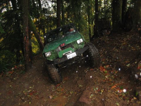 1990 Ford Bronco - Off-road SUV navigates a challenging muddy trail through a dense forest environment.