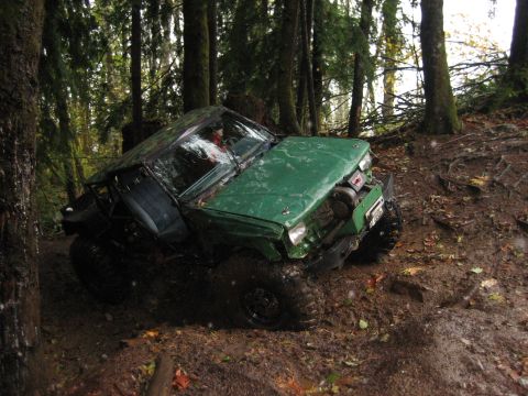 1990 Ford Bronco - A green off-road vehicle navigates a challenging muddy path through a dense forest.