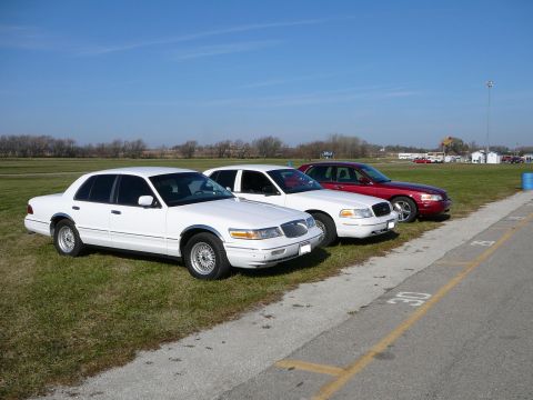 1997 Mercury Grand Marquis - Three sedans, including a white 1997 Mercury Grand Marquis, are parked in a line on a grassy area next to a paved surface.