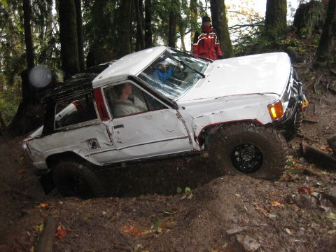1990 Ford Bronco - White SUV is shown off-roading on a wet, wooded trail with mud and fallen leaves.