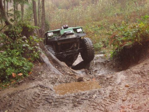 1990 Ford Bronco - An off-road vehicle navigates a challenging muddy terrain with steep inclines and fallen logs.