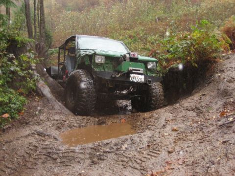 1990 Ford Bronco - This heavily modified off-road vehicle tackles a challenging muddy terrain with its large tires and winch.