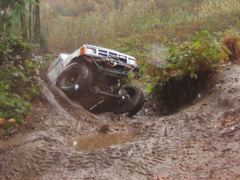 1990 Ford Bronco - An off-road SUV navigates a challenging muddy terrain with steep inclines and dense foliage.