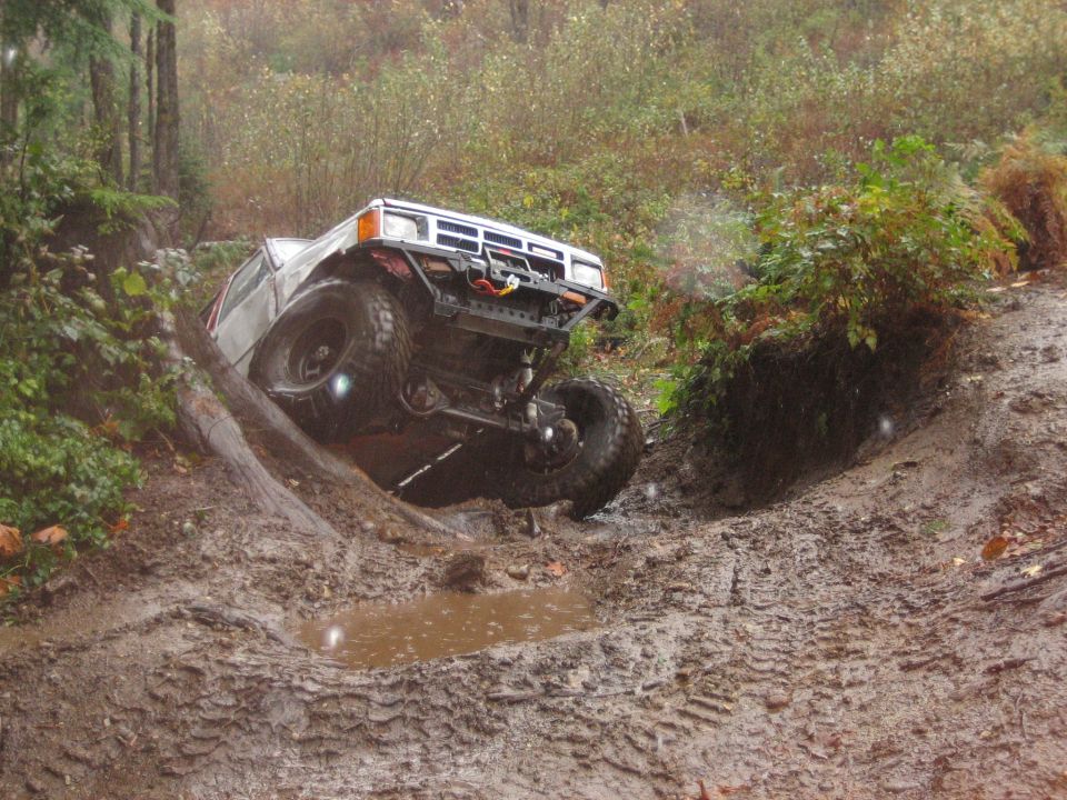 White off-road SUV climbing a muddy hill, front grille and bumper visible