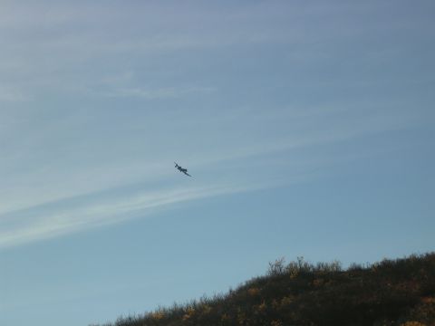 1982 Chevrolet C/K Pickup - An airplane is seen flying in the distance against a clear blue sky with some clouds.