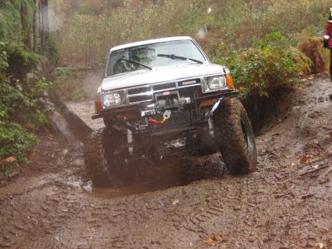 1990 Ford Bronco - Modified Toyota pickup truck tackling a challenging muddy off-road course.