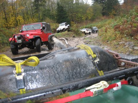 1990 Ford Bronco - Several Jeeps navigate a challenging muddy off-road trail with a red Jeep Wrangler leading the way.