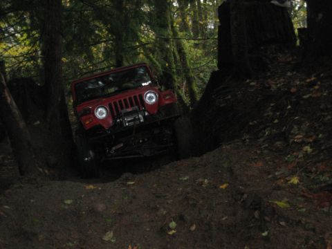 1990 Ford Bronco - A red Jeep Wrangler navigates a challenging off-road trail through a wooded area.