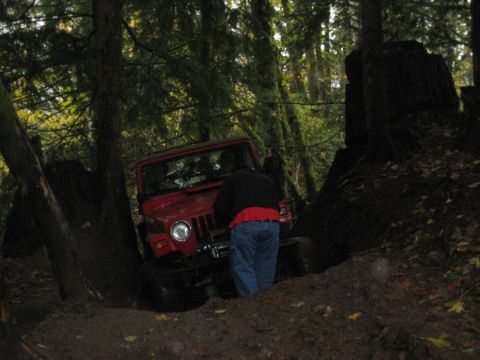 1990 Ford Bronco - A red Jeep Wrangler navigates a muddy, wooded trail with a person observing.