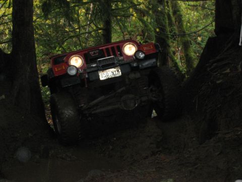 1990 Ford Bronco - A red Jeep Wrangler navigates a challenging muddy trail in a forest setting.