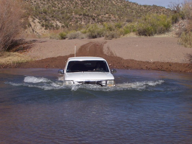 White Ford Bronco crossing deep water in the desert, bow wave over the front bumper