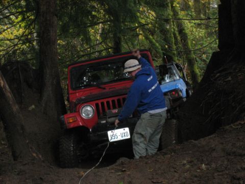 1990 Ford Bronco - A red Jeep Wrangler is stuck in the mud, with a person winching it out, while another vehicle is visible behind it.