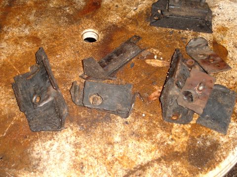 1989 Ford Bronco - Several corroded metal brackets and rubber mounts are scattered across a stained surface.
